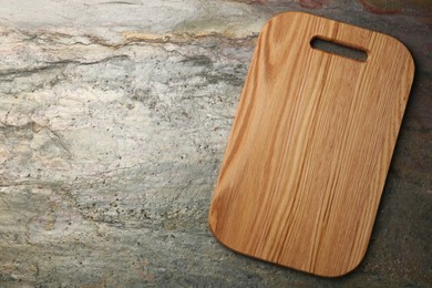 Photo of Wooden cutting board on textured table, top view. Space for text
