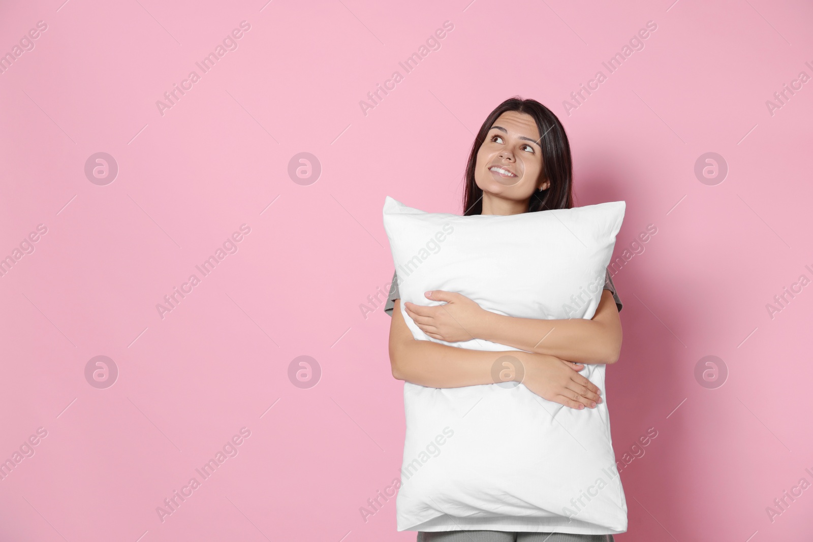 Photo of Happy young woman hugging soft pillow on pink background, space for text