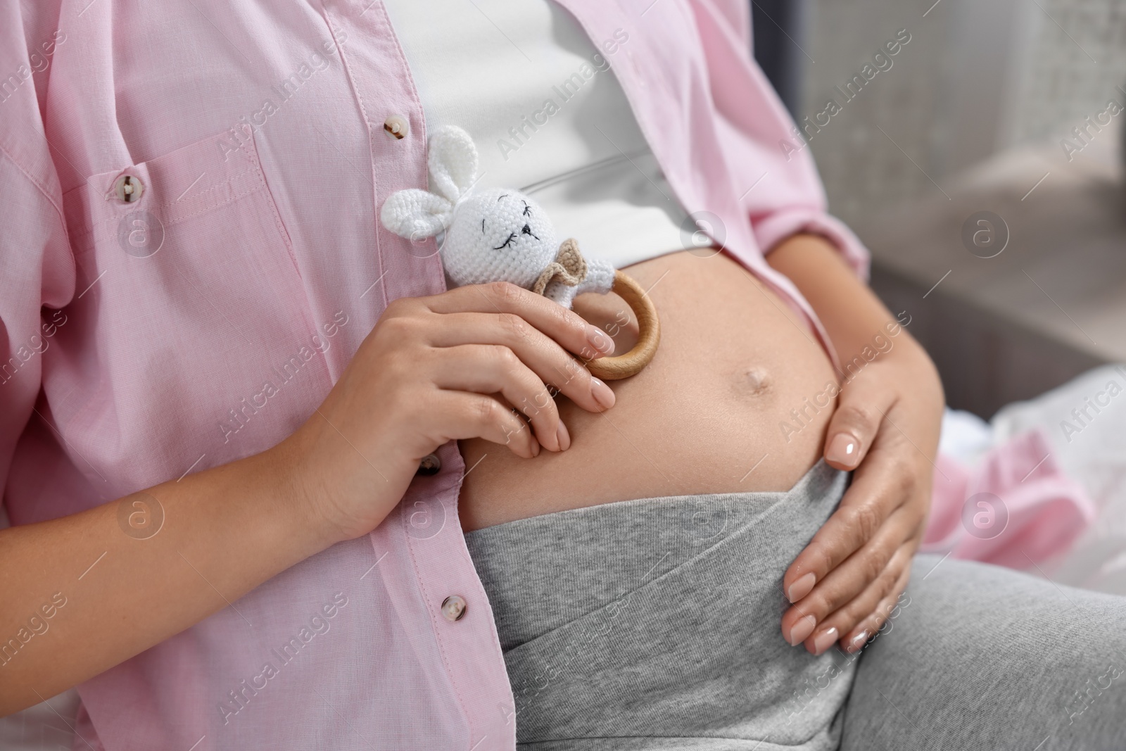 Photo of Pregnant woman with bunny toy lying on bed indoors, closeup