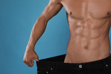 Photo of Shirtless man with slim body wearing big jeans on light blue background, closeup