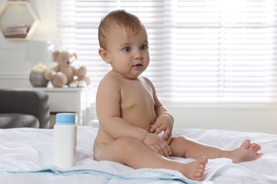 Photo of Adorable little baby with bottle of dusting powder on bed at home
