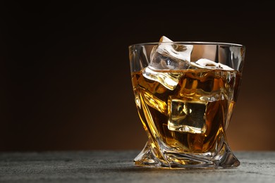 Photo of Whiskey and ice cubes in glass on grey textured table, closeup. Space for text