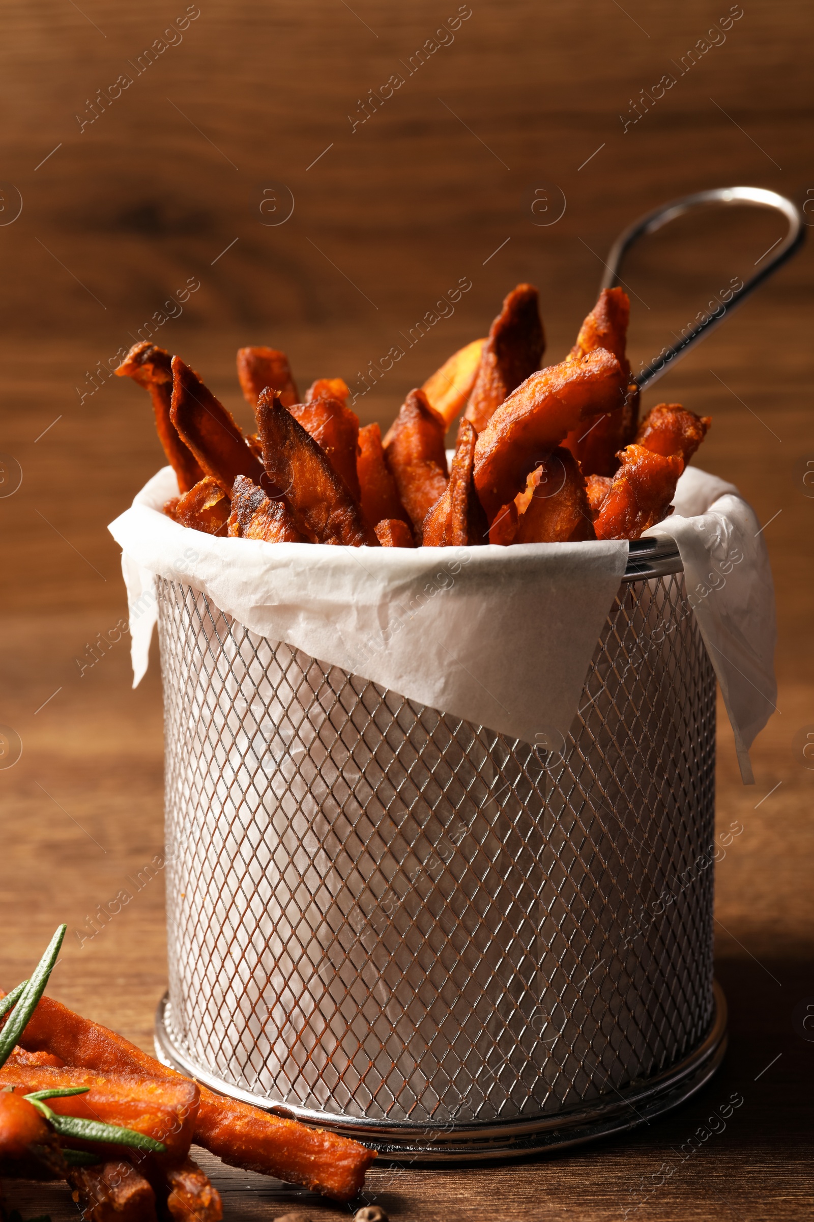 Photo of Frying basket with sweet potato fries on wooden table, closeup