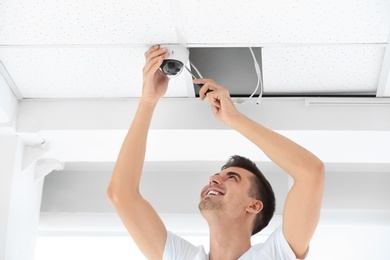 Technician installing CCTV camera on ceiling indoors