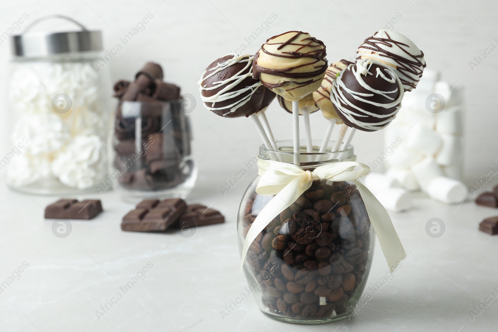 Photo of Yummy cake pops coated with chocolate in glass jar full of coffee beans on table. Space for text