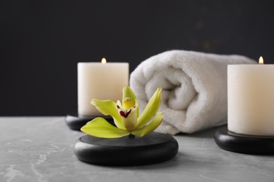 Photo of Spa stones with exotic flower and burning candles on grey table against dark background, space for text