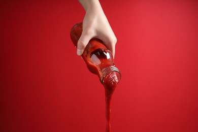 Woman pouring tasty ketchup from bottle on red background, closeup