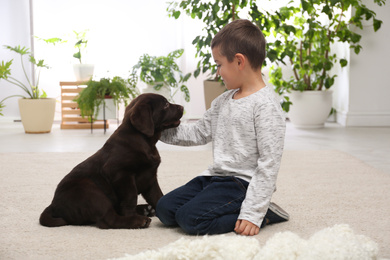 Photo of Little boy playing with puppy at home. Friendly dog