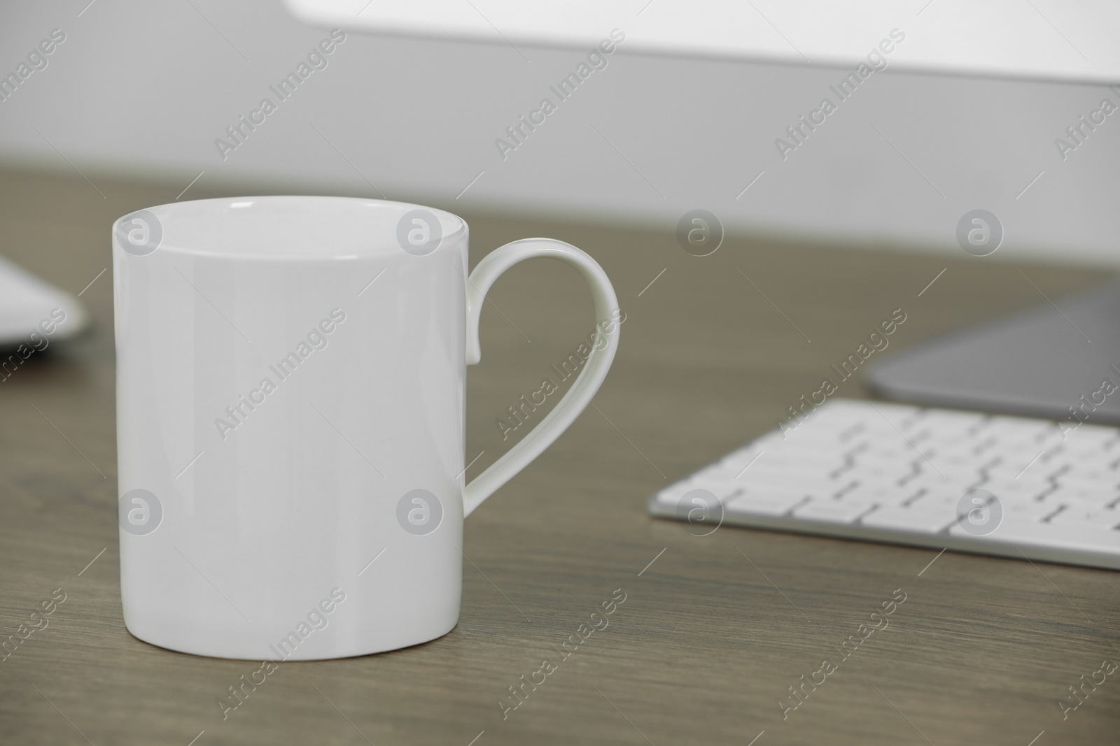 Photo of White ceramic mug on wooden table at workplace. Mockup for design