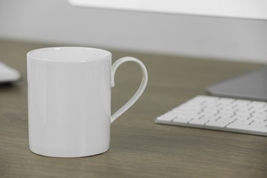 White ceramic mug on wooden table at workplace. Mockup for design