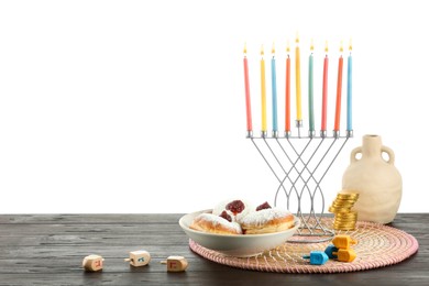 Photo of Hanukkah celebration. Composition with menorah, dreidels and donuts on black wooden table against white background