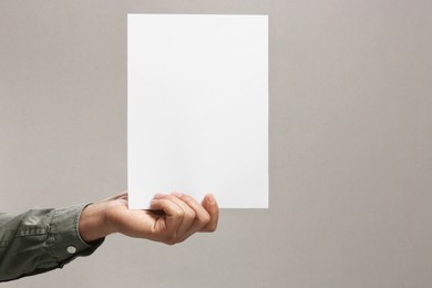 Man holding sheet of paper on grey background, closeup. Mockup for design