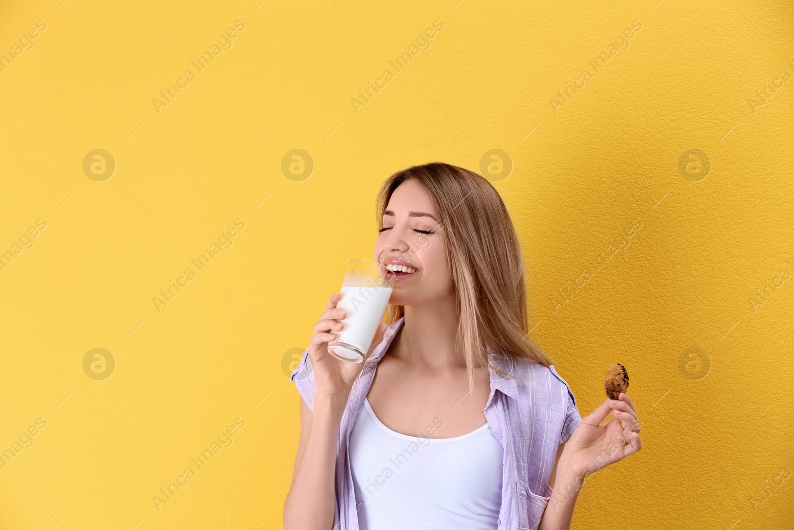 Photo of Beautiful young woman drinking milk with cookie on color background