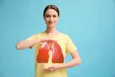 Young woman holding hands near chest with illustration of lungs on turquoise background, closeup