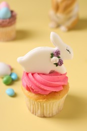 Photo of Tasty cupcake with Easter decor on pale yellow background, closeup