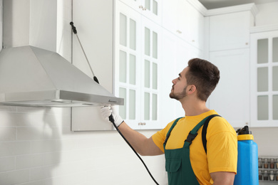 Photo of Pest control worker spraying insecticide on furniture in kitchen