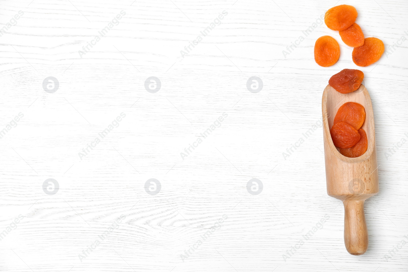 Photo of Wooden scoop of dried apricots on white table, top view with space for text. Healthy fruit