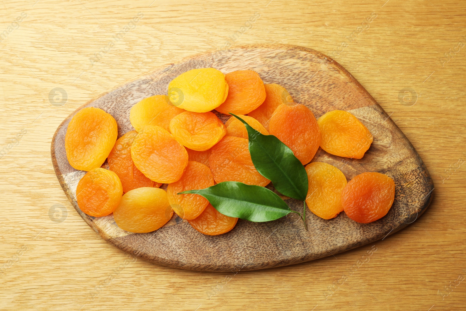 Photo of Tasty apricots and green leaves on wooden table, top view. Dried fruits