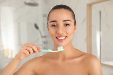 Woman holding toothbrush with paste in bathroom