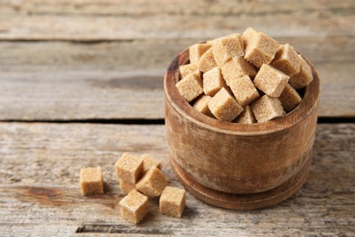 Photo of Bowl with brown sugar cubes on wooden table, closeup. Space for text