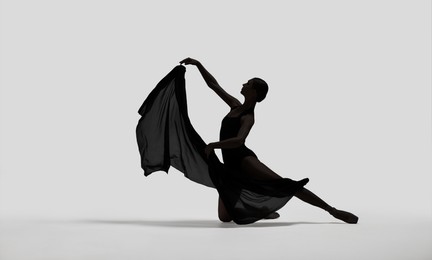 Beautiful ballerina with veil dancing on light background. Dark silhouette of dancer