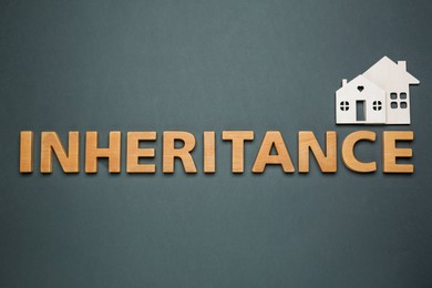 Photo of Word Inheritance made with wooden letters and houses model on black background, flat lay