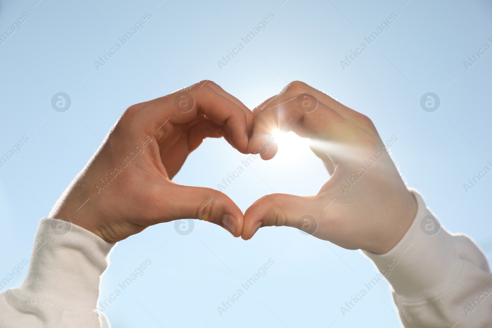 Photo of Man showing heart against blue sky outdoors on sunny day, closeup of hands