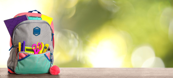 Image of Bright backpack with school stationery on table against blurred green background. Space for text