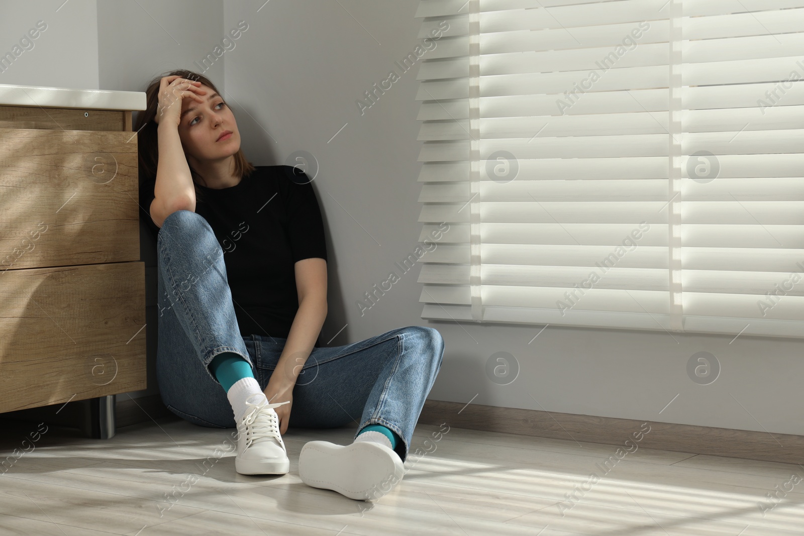 Photo of Sad young woman sitting on floor indoors, space for text