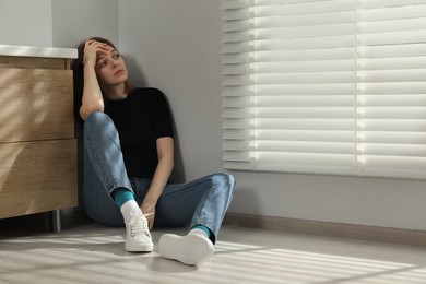 Sad young woman sitting on floor indoors, space for text