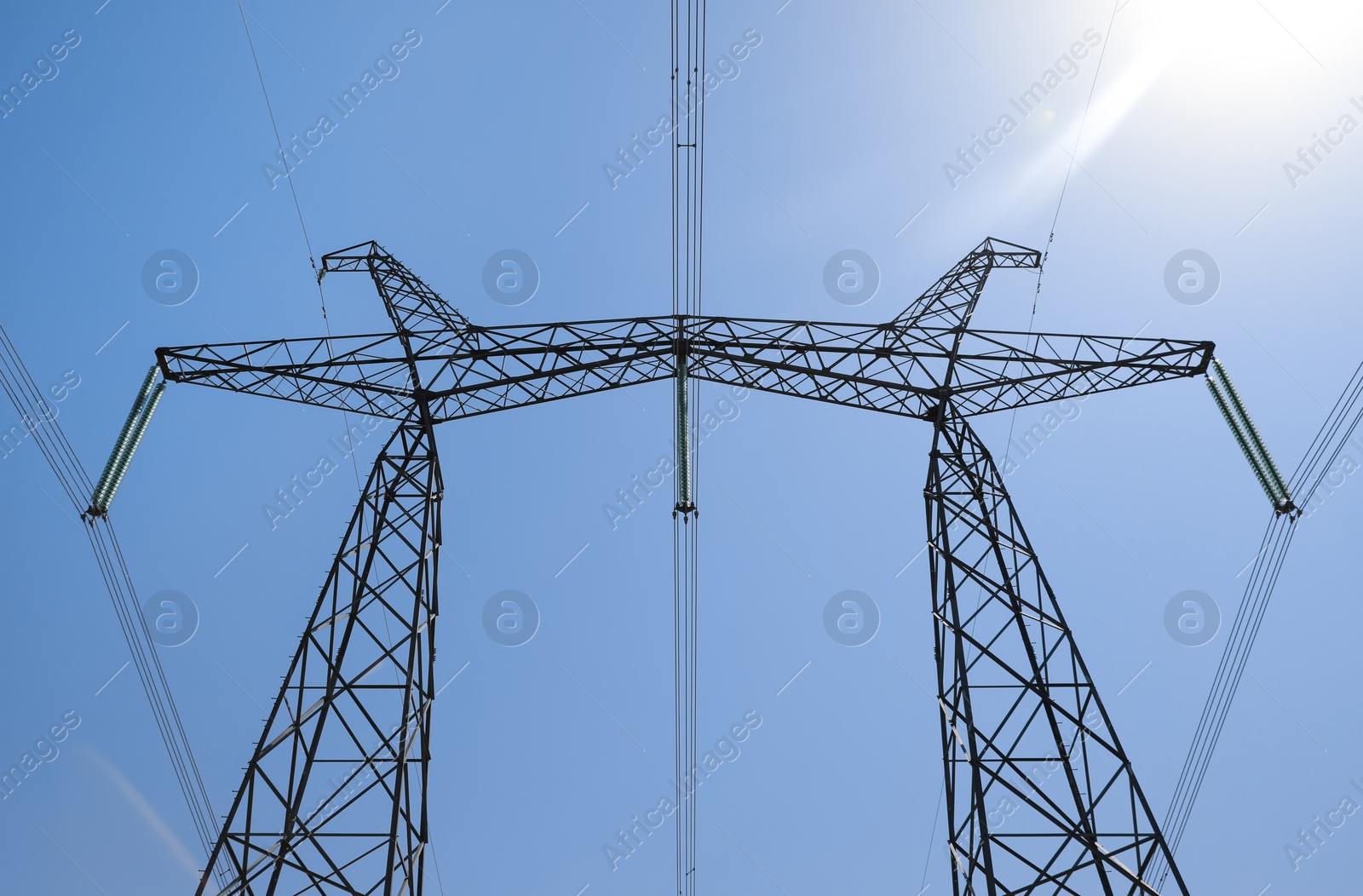 Photo of High voltage tower with electricity transmission power lines against blue sky, low angle view