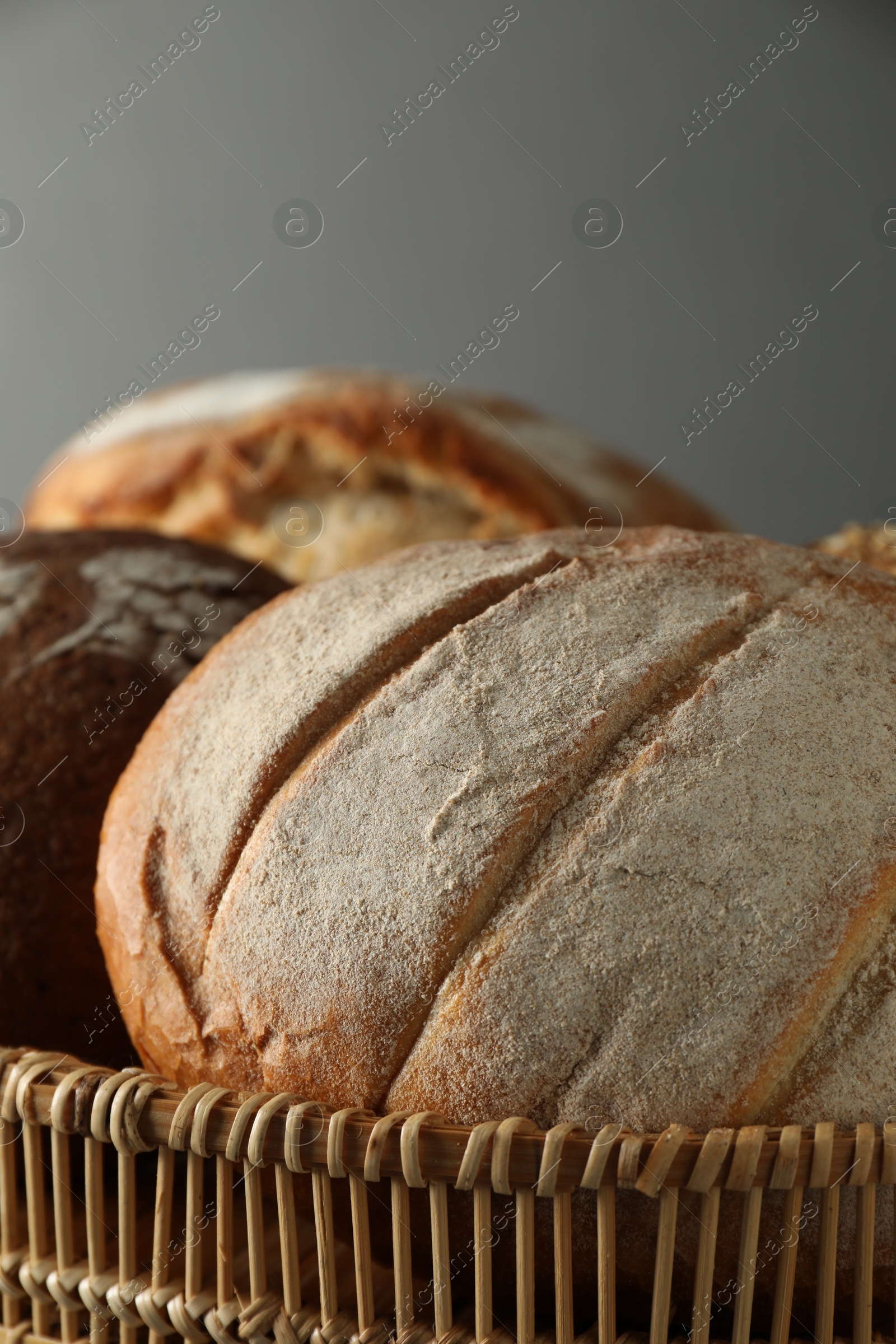 Photo of Wicker basket with different types of fresh bread against grey background, closeup