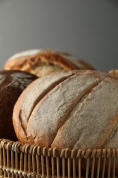 Photo of Wicker basket with different types of fresh bread against grey background, closeup