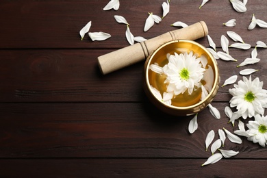 Photo of Flat lay composition with golden singing bowl, flowers and mallet on wooden table, space for text. Sound healing