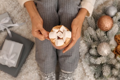 Young woman with cocoa sitting on light blanket, top view. Christmas holiday