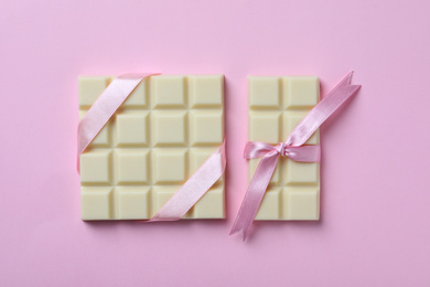 Tasty white chocolate with ribbons on pink background, flat lay