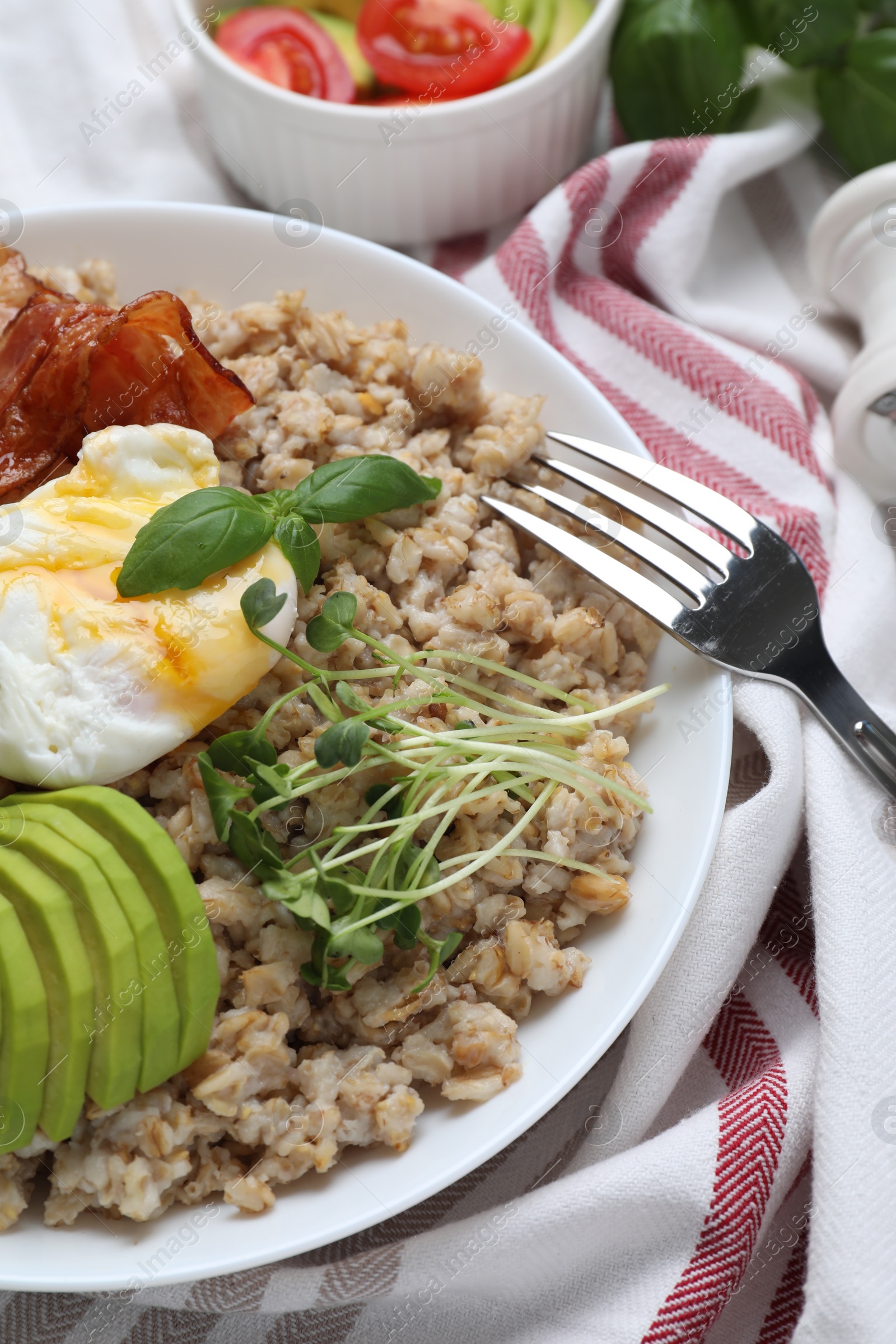 Photo of Delicious boiled oatmeal with poached egg, bacon, avocado and microgreens on table, closeup