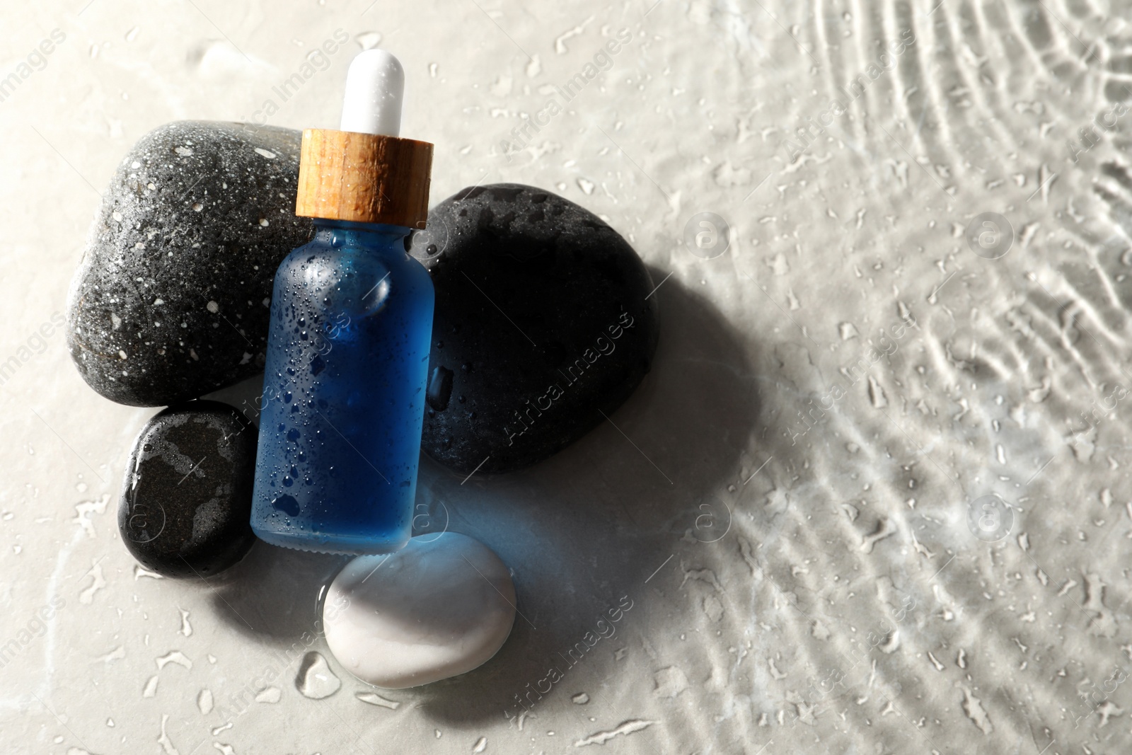 Photo of Bottle of face serum and spa stones in water on light background, space for text