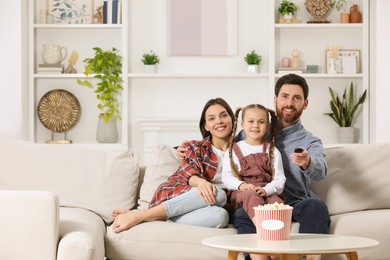 Happy family watching TV with popcorn on sofa at home, space for text