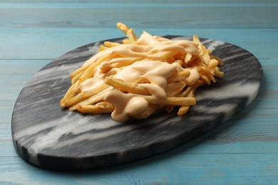 Photo of Delicious French fries with cheese sauce on light blue wooden table, closeup