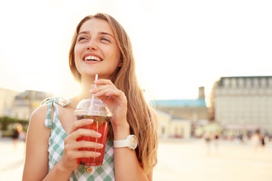 Young woman with refreshing drink on city street. Space for text