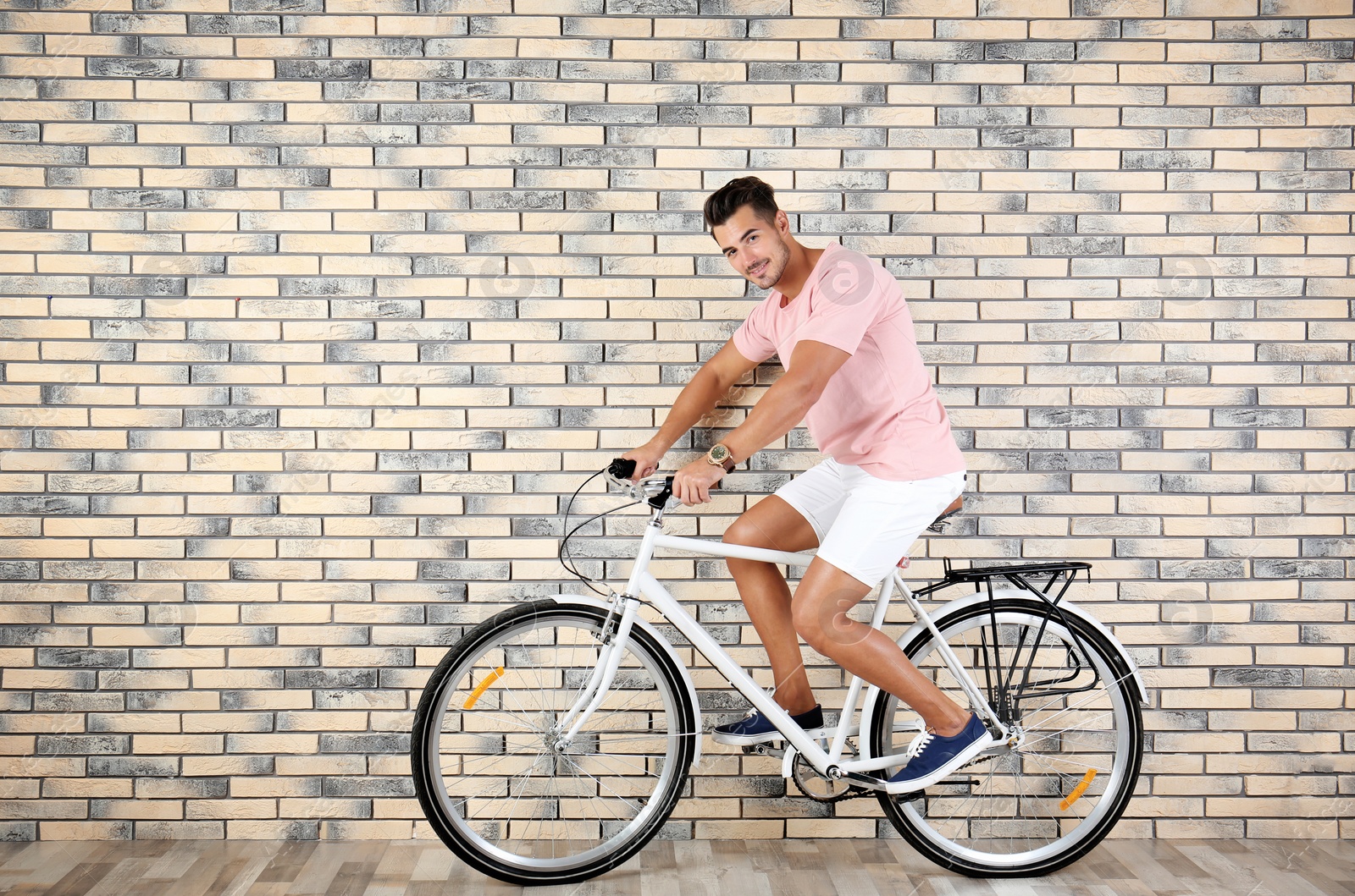 Photo of Handsome young hipster man riding bicycle near brick wall