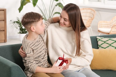 Photo of Little boy presenting his mother with gift on sofa at home