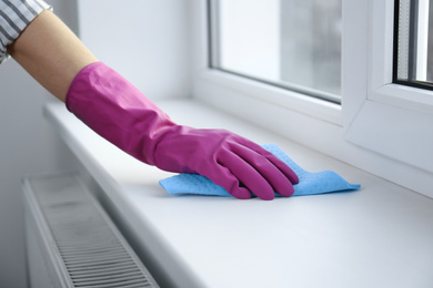 Photo of Woman cleaning window sill with rag indoors, closeup