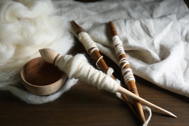 Photo of Spindles and soft white wool on wooden table
