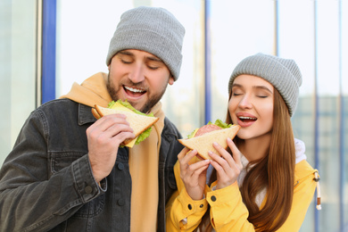 Photo of Happy young couple with sandwiches on city street