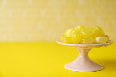 Photo of Delicious lemon drops on yellow table. Space for text