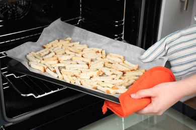 Photo of Woman taking baking pan with hard chucks out of oven, closeup