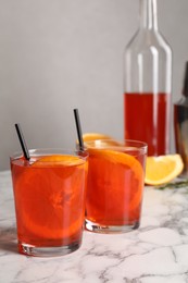 Photo of Aperol spritz cocktail, orange slices and straws in glasses on white marble table
