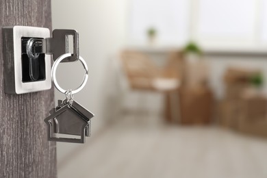 Photo of Mortgage and real estate. Open door with key and house shaped keychain against blurred background, space for text